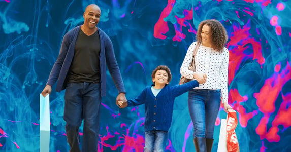 A Black man, woman, and little boy smiling and walking, holding shopping bags.